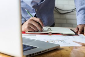 a man's hands at a computer with a notepad and graphs